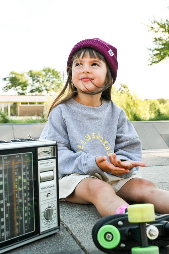 petite fille avec des rollers dans un skatepark, sweat gris oversize streetwear unisexe en coton bio et un bonnet pour enfant en laine couleur prune