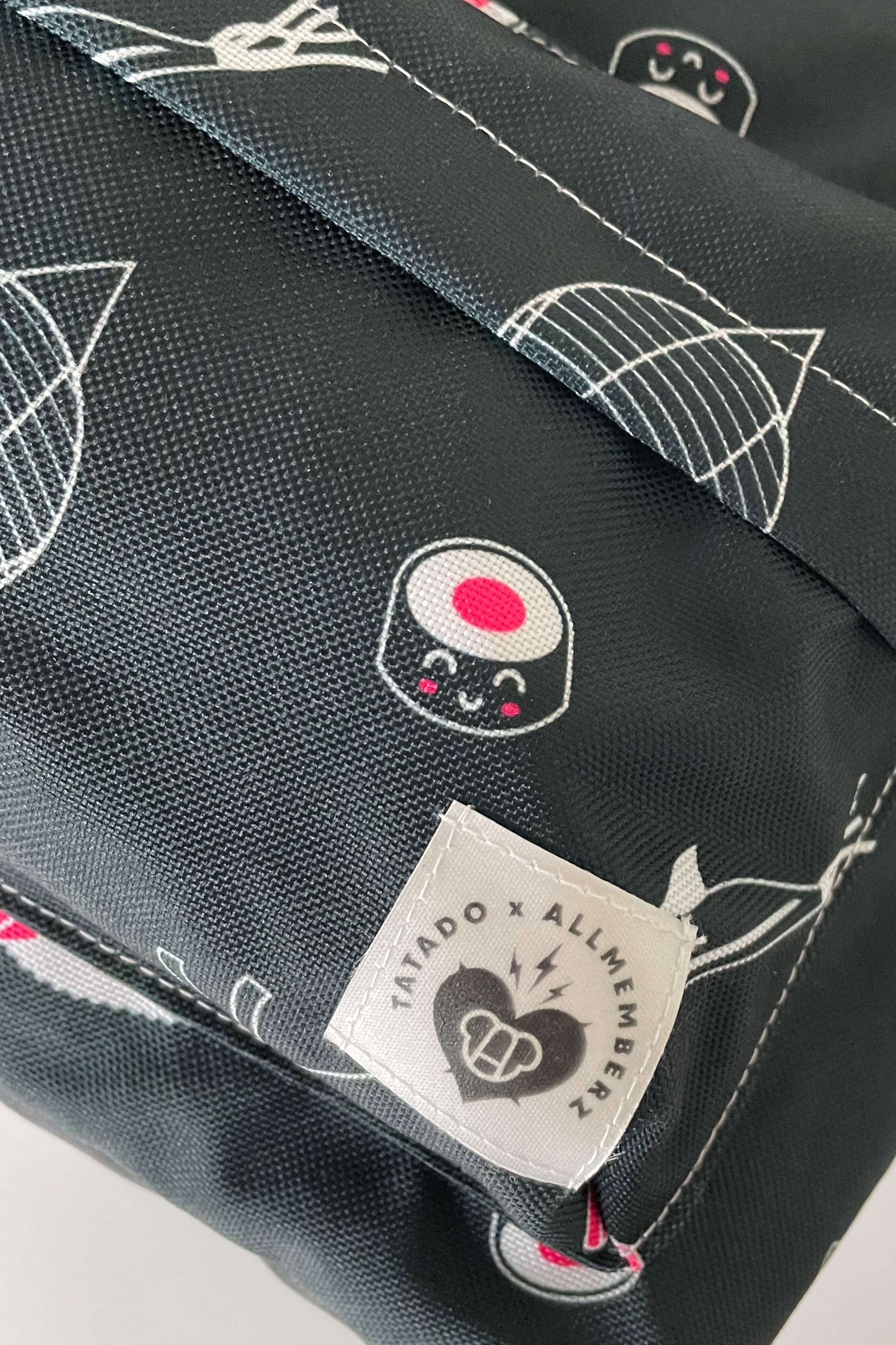 sac à dos pour enfant motif Tokyo joyeux et coloré sur fond noir, dessins de sushis style manga, vue en gros plan sur poche zippée, tissu toile imperméable